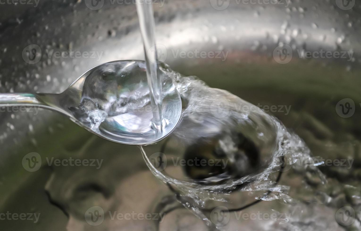 Running water from a water tap into the drain of a chrome sink. photo