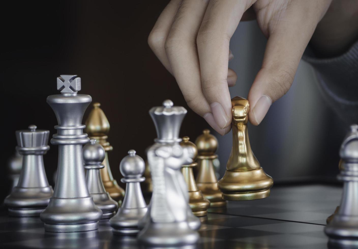 Hand businessman moving the golden knight chess fighting silver knight with fire sparks chess on chess board to successfully in the competition. Management or leadership strategy and teamwork concept. photo