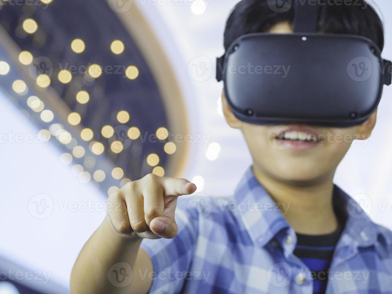 Kid wearing virtual reality glasses in modern interior design studio and trying to touch dots network and earth map or something appear in VR with exciting.Flares effect, blurred background concept. photo