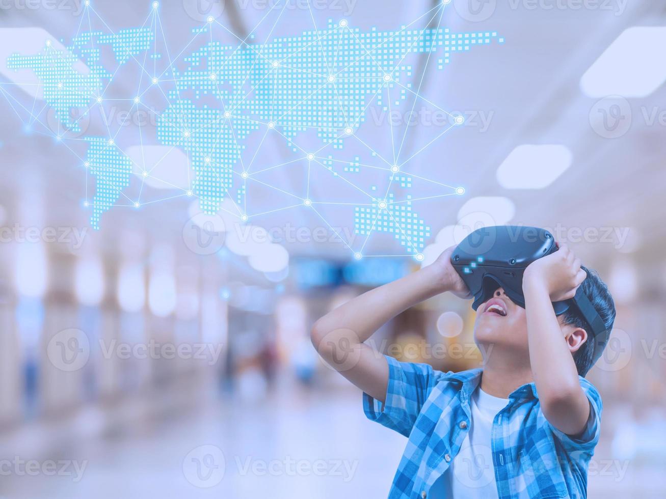 Boy wearing virtual reality glasses in modern interior design studio and trying to touch dots network and earth map or something appear in VR with exciting.Flares effect, blurred background concept. photo