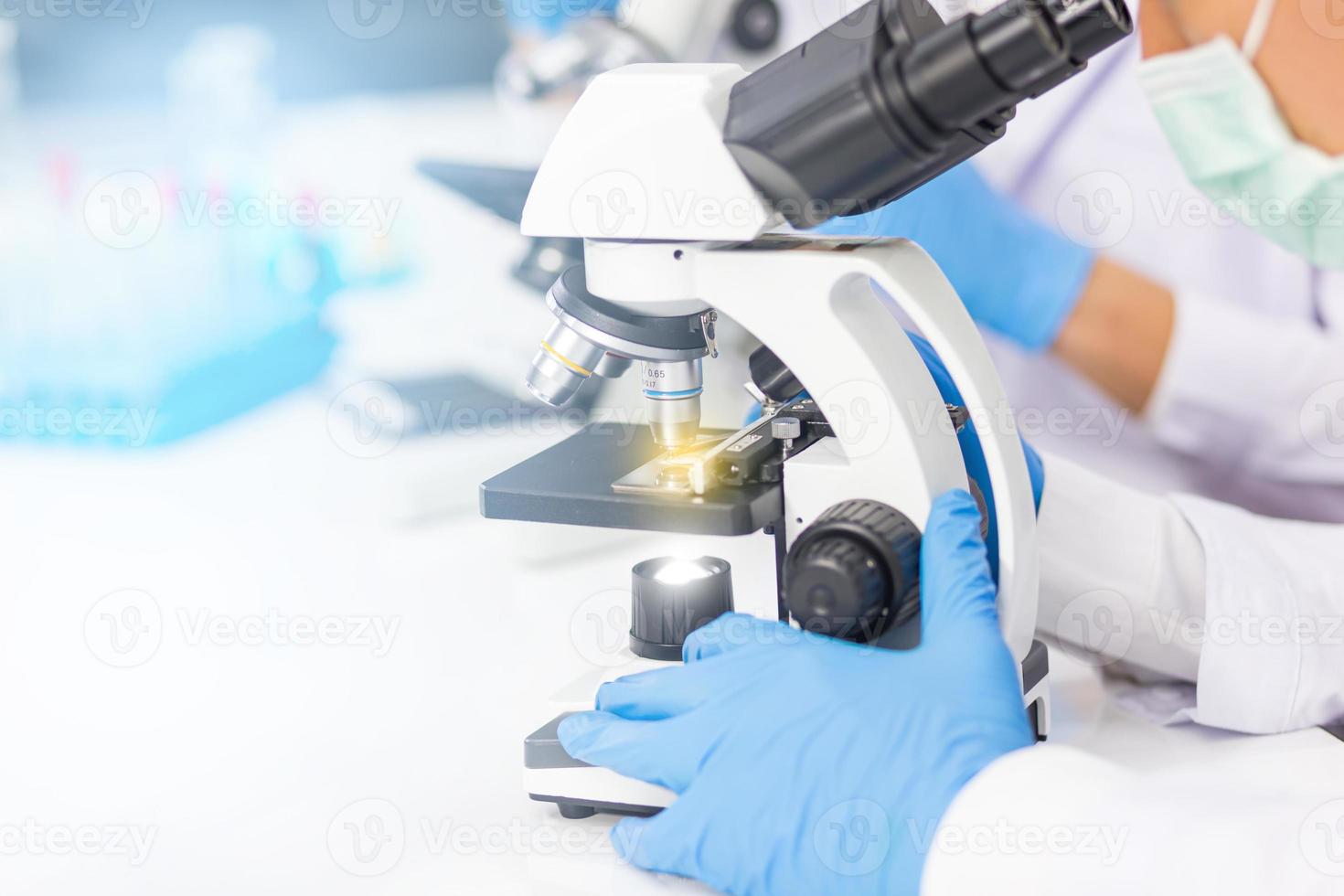 las manos de los hombres que usan guantes de goma azules están usando un microscopio para trabajar en el laboratorio. foto