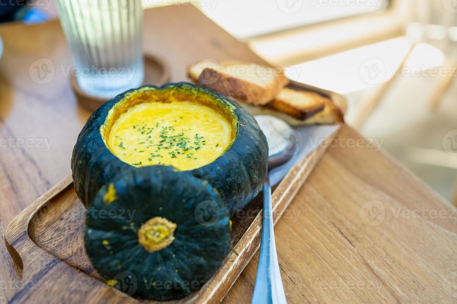 Roasted pumpkin cream soup in raw pumpkin serve with bread on rustic wooden background. photo