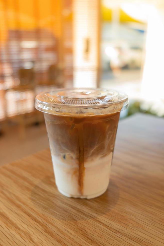 café con leche helado preparado en frío, que se muestra separado en una capa en la parte inferior como la parte superior de la leche junto al café en un vaso de plástico sobre una mesa de madera en el restaurante y la cafetería foto