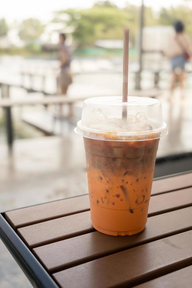 té con leche helado, café con leche mezclado, que se muestra separado en una capa en la parte inferior como el té con leche junto al café con leche en un vaso de plástico sobre una mesa de madera en el restaurante y la cafetería foto