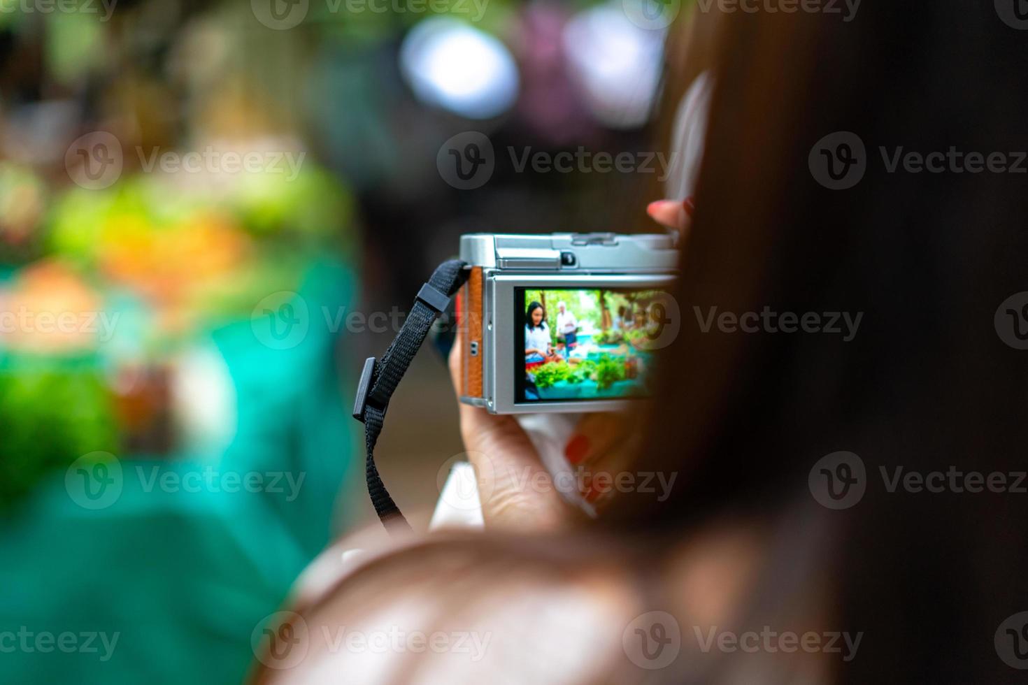 The woman holds the vintage camera, taking a photo of the local vegetable market.