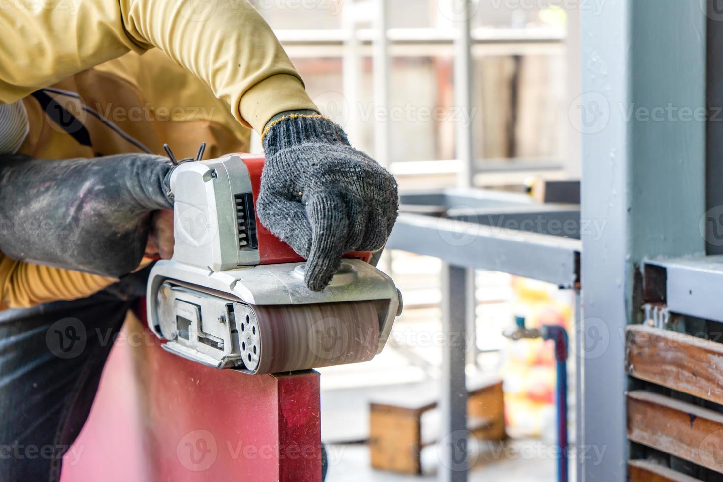 Carpenter is shaving red wood door by his shaving machine in outdoor field with steel pole building structure environment. photo