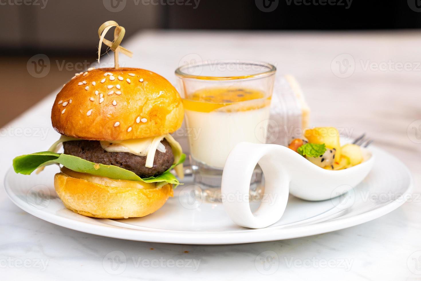 pequeña hamburguesa y pudín de maracuyá en vaso con frutas mixtas y envolturas de sandwish en un plato blanco para el tiempo de descanso del seminario. foto