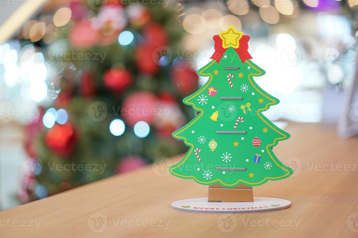 decoración artesanal de papel del árbol de navidad en la parte trasera en la mesa de madera con un gran árbol de navidad borroso detrás. foto