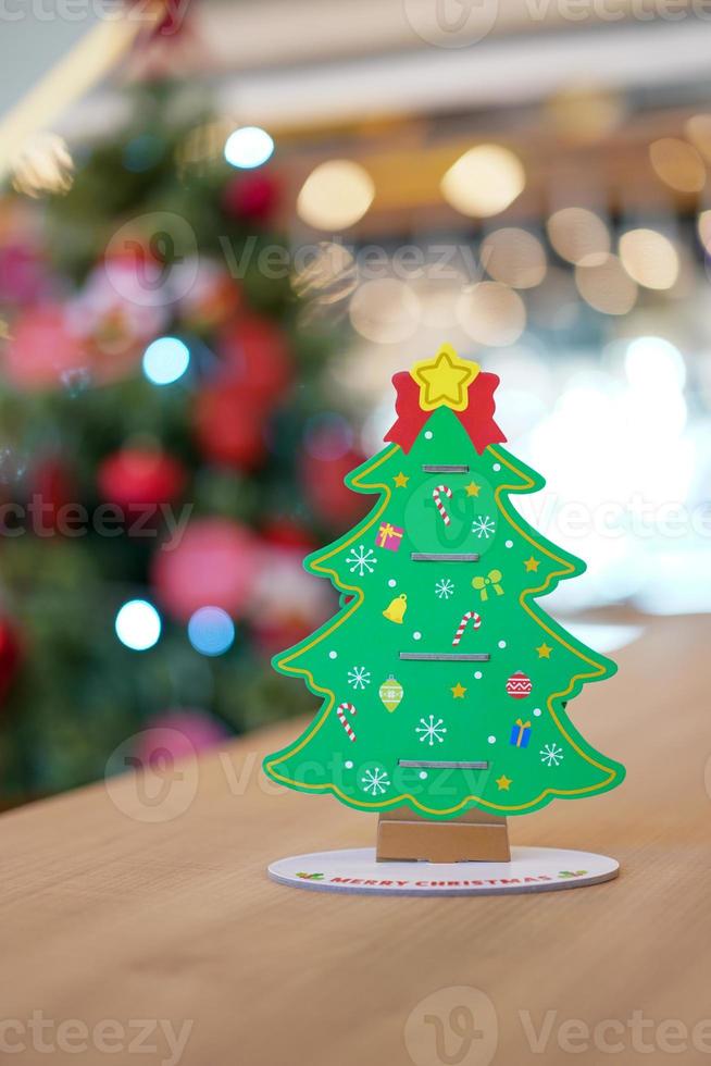 Backside Christmas tree paper craft decoration on the wood table with blur big Christmas tree behide. photo