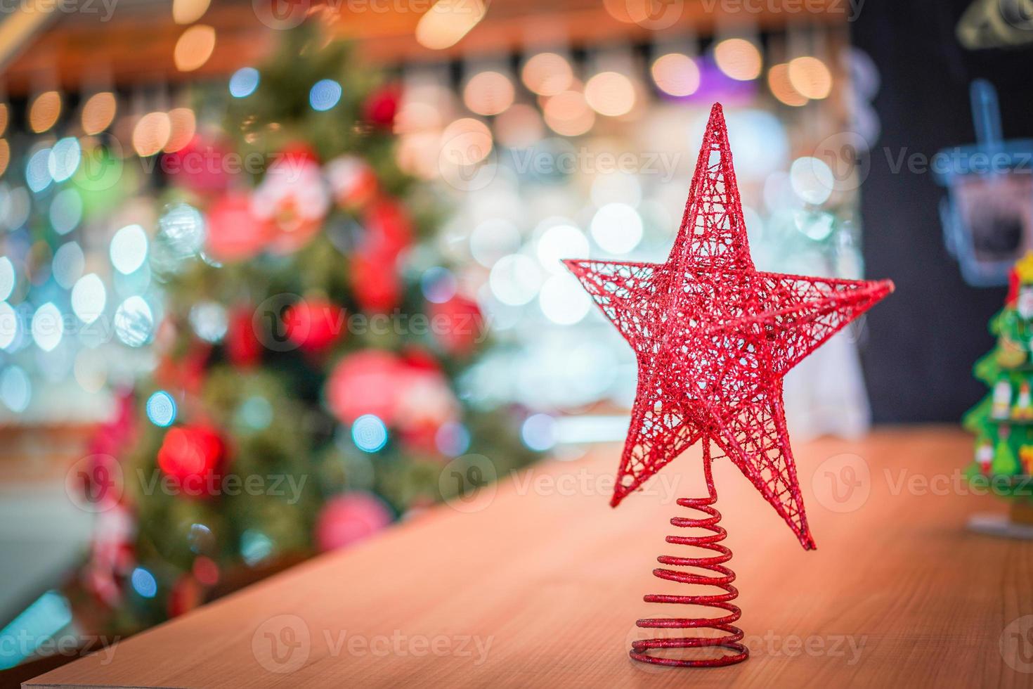 Red star decoration on the wood table with blur big Christmas tree behide. photo