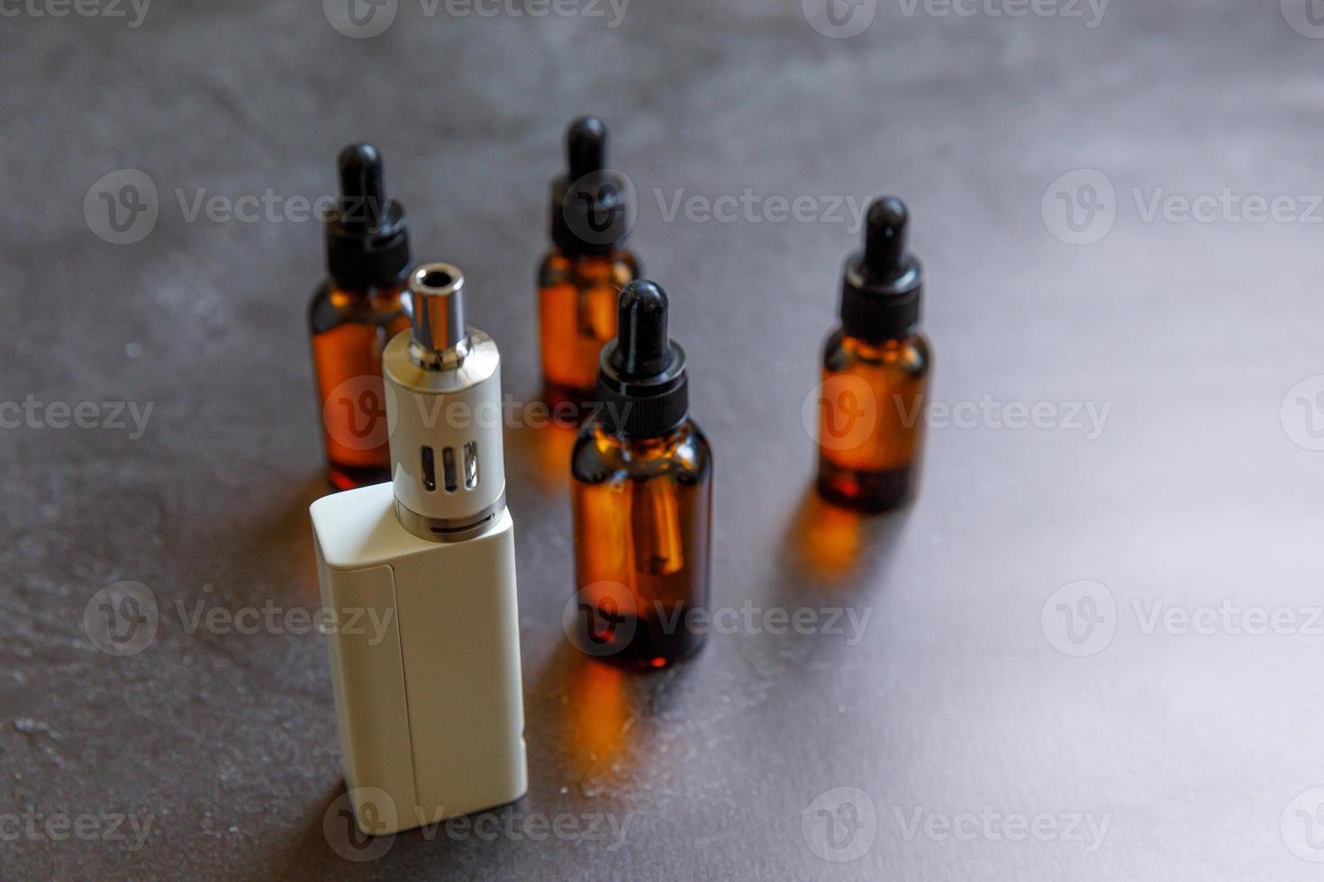 Vaping device e-cigarette electronic cigarette and liquid bottles on dark black stone shale background. Vape device for alternative smoking. Vaping shop concept. Gadget for vaper. Vaping accessories. photo