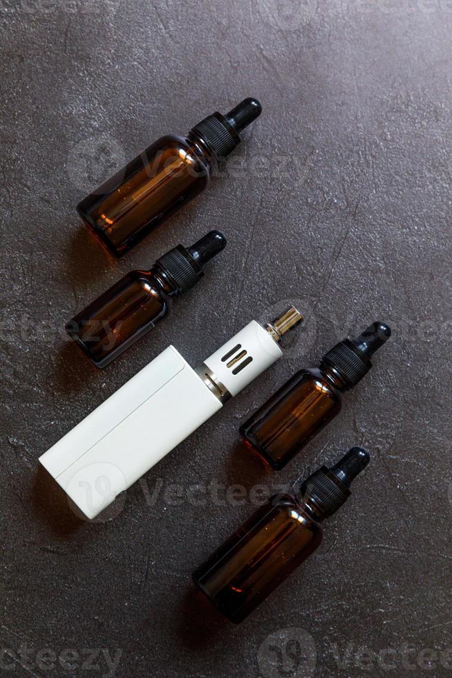 Vaping device e-cigarette electronic cigarette and liquid bottles on dark black stone shale background. Vape device for alternative smoking. Vaping shop concept. Gadget for vaper. Vaping accessories. photo