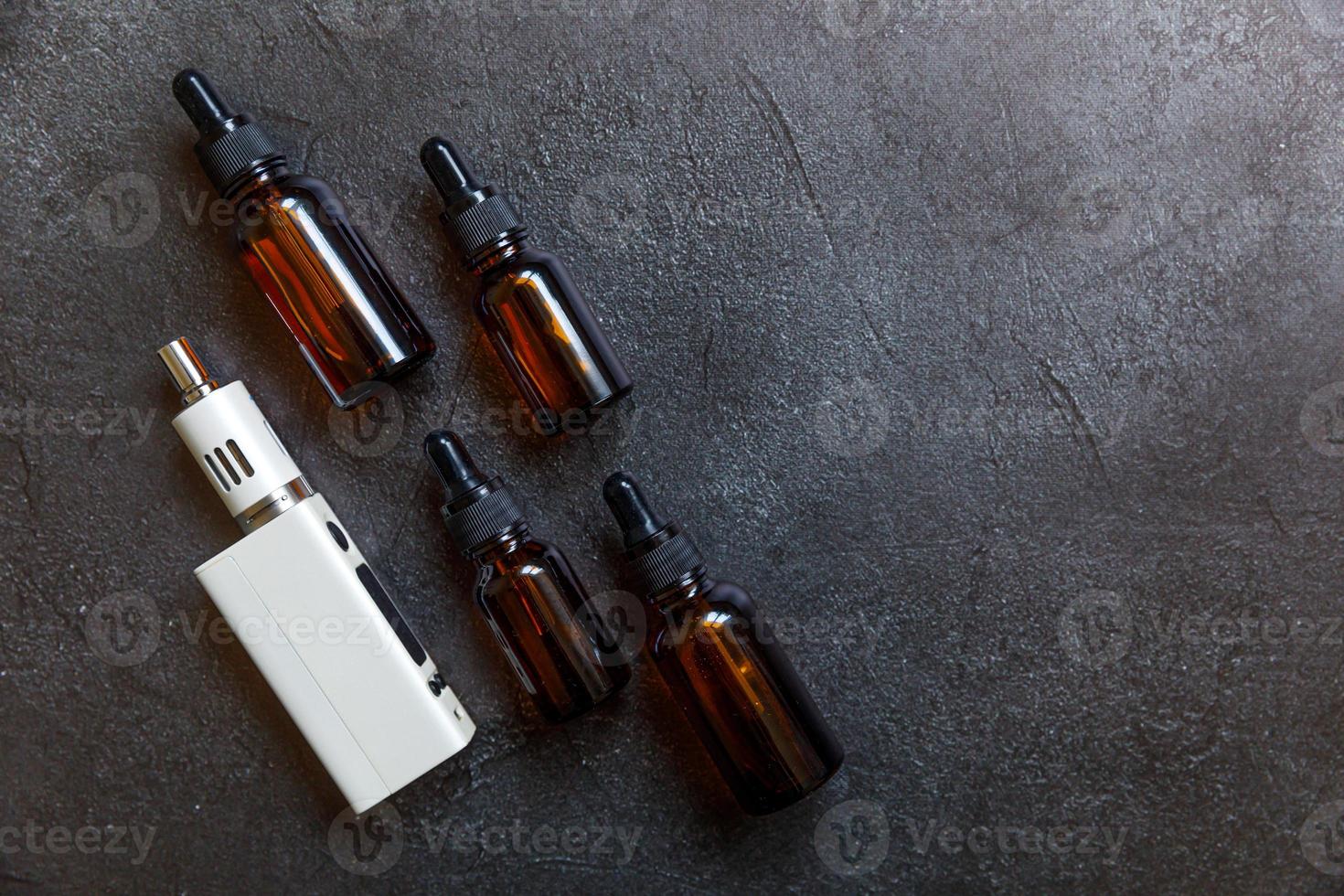 Vaping device e-cigarette electronic cigarette and liquid bottles on dark black stone shale background. Vape device for alternative smoking. Vaping shop concept. Gadget for vaper. Vaping accessories. photo