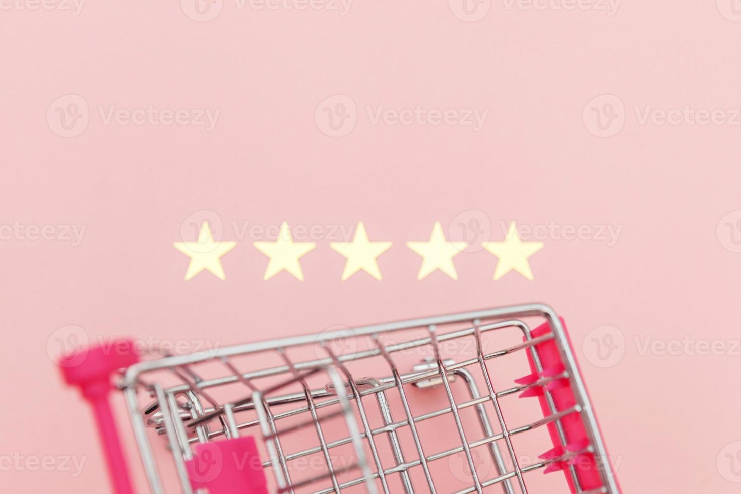 Small supermarket grocery push cart for shopping toy with wheels and 5 stars rating isolated on pastel pink background. Retail consumer buying online assessment and review concept. photo