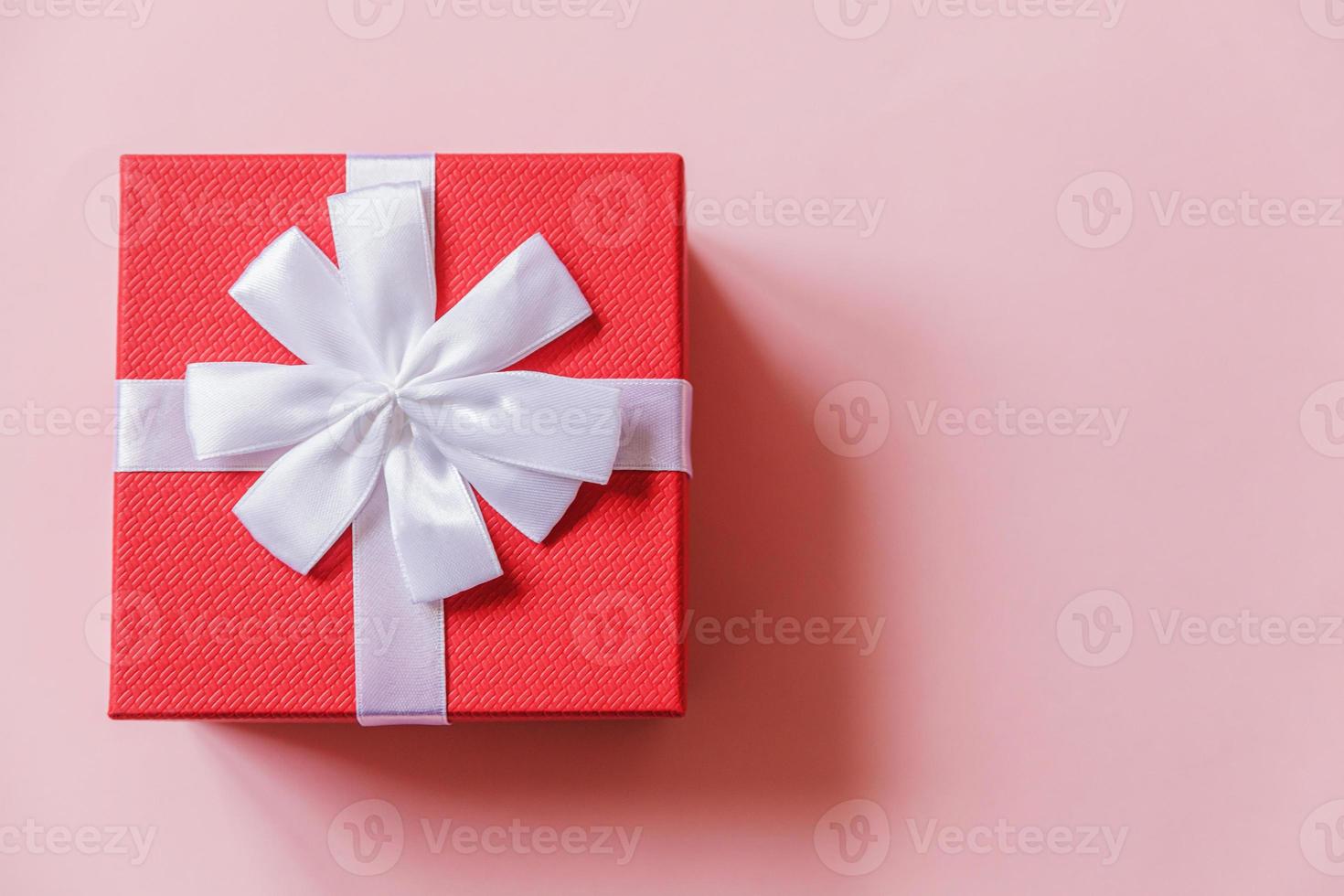 Christmas New Year birthday valentine celebration present romantic concept. Simply minimal design red gift box isolated on pastel pink colorful background. Flat lay top view, copy space photo