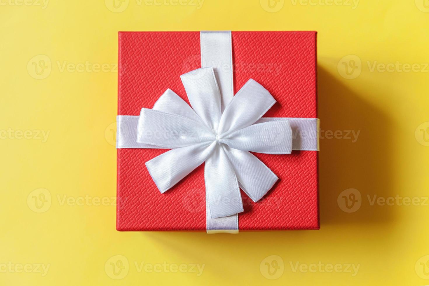 Christmas New Year birthday valentine celebration present romantic concept. Simply minimal design red gift box isolated on yellow colorful background. Flat lay top view copy space. photo