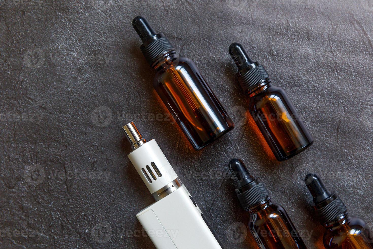 Vaping device e-cigarette electronic cigarette and liquid bottles on dark black stone shale background. Vape device for alternative smoking. Vaping shop concept. Gadget for vaper. Vaping accessories. photo
