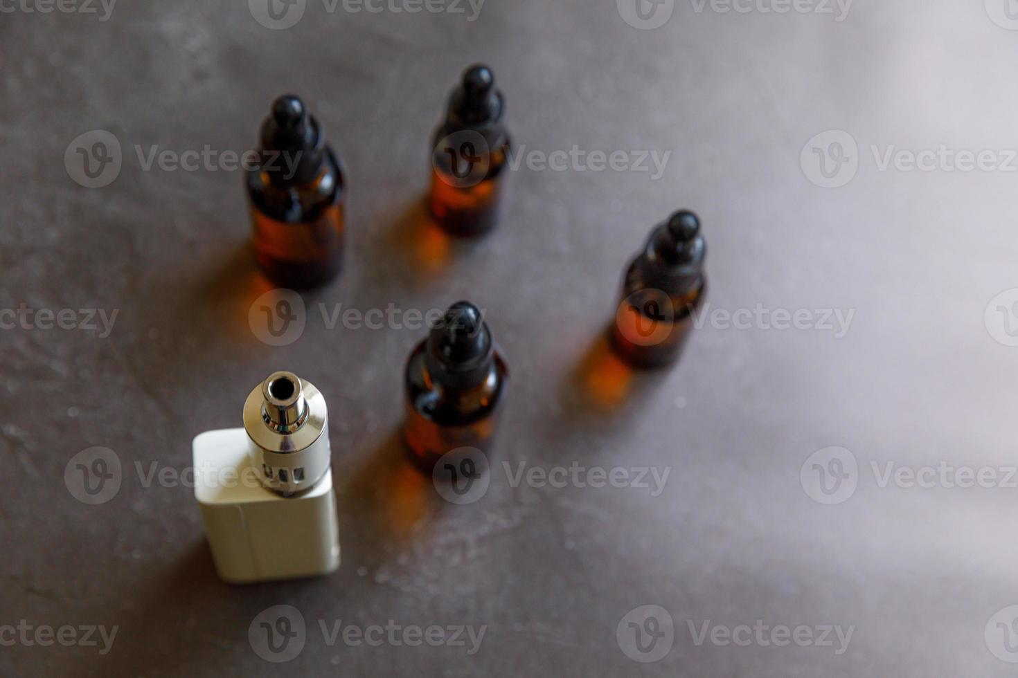 Vaping device e-cigarette electronic cigarette and liquid bottles on dark black stone shale background. Vape device for alternative smoking. Vaping shop concept. Gadget for vaper. Vaping accessories. photo
