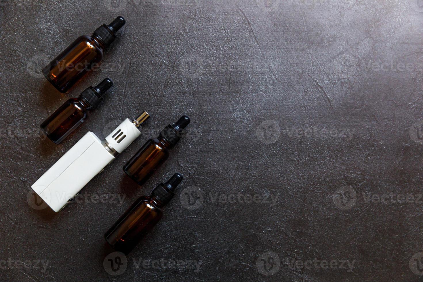Vaping device e-cigarette electronic cigarette and liquid bottles on dark black stone shale background. Vape device for alternative smoking. Vaping shop concept. Gadget for vaper. Vaping accessories. photo