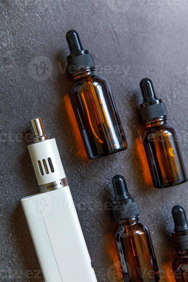 Vaping device e-cigarette electronic cigarette and liquid bottles on dark black stone shale background. Vape device for alternative smoking. Vaping shop concept. Gadget for vaper. Vaping accessories. photo