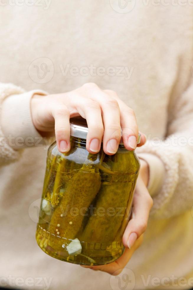 mujer ama de casa mano sosteniendo un tarro de cristal de pepinos encurtidos. preparación doméstica decapado y enlatado de verduras, alimentos orgánicos de invierno. comida casera fermentada saludable pepinos marinados en tarro. foto