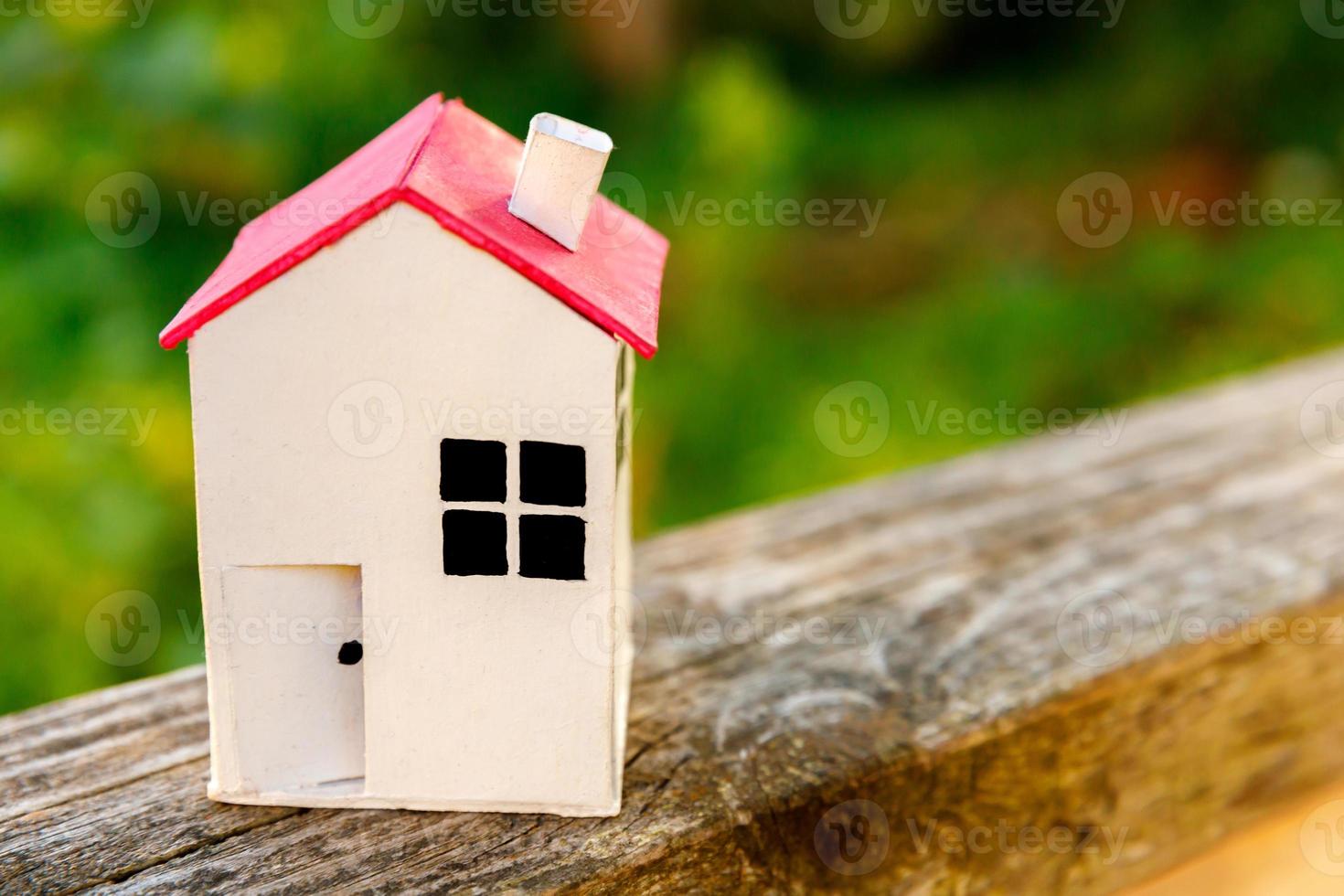 Miniature white toy model house in wooden background near green backdrop. Eco Village, abstract environmental background. Real estate mortgage property insurance dream home ecology concept. photo