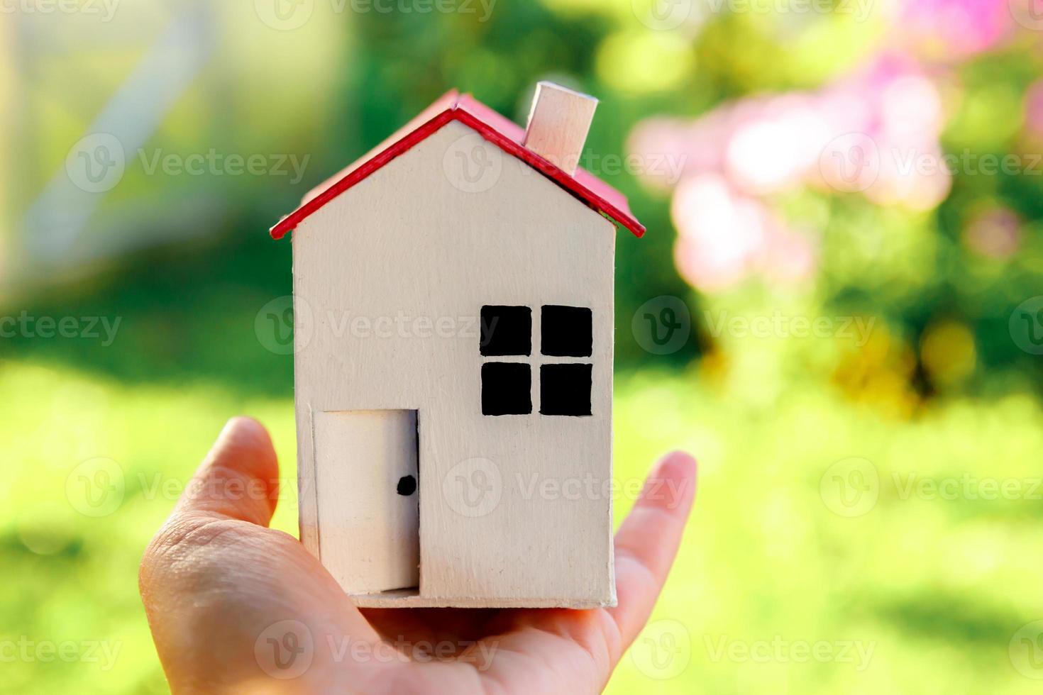 casa modelo en miniatura en mano de mujer sobre fondo verde al aire libre. aldea ecológica, fondo ambiental abstracto. concepto de ecología de casa de ensueño de seguro de propiedad de hipoteca de bienes raíces. foto