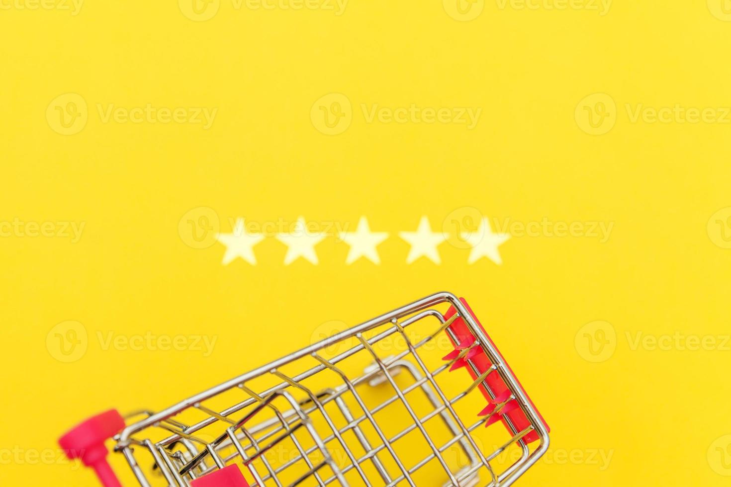 Small supermarket grocery push cart for shopping toy with wheels and 5 stars rating isolated on yellow background. Retail consumer buying online assessment and review concept. photo