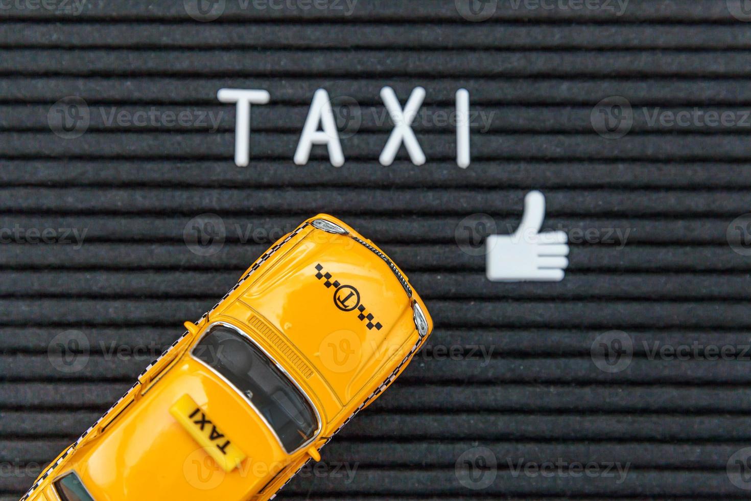 Simply design yellow toy car Taxi Cab model with inscription TAXI letters word on black background. Automobile and transportation symbol. City traffic delivery urban service idea concept. Copy space. photo