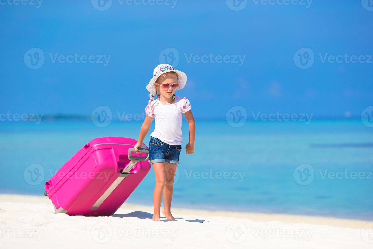 Little adorable girl with big suitcase on tropical white beach photo