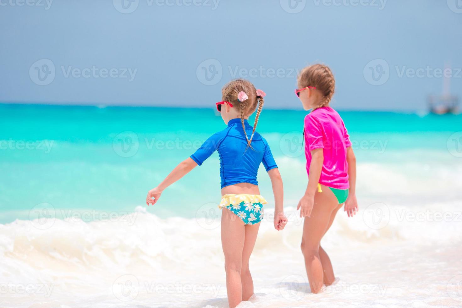 Adorable little girls at beach having fun in shallow water during summer vacation photo