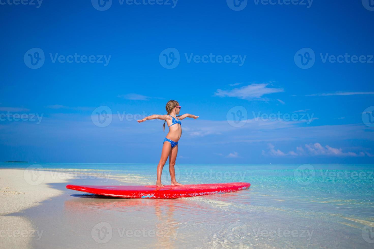 Little adorable girl practice surfing position at beach photo