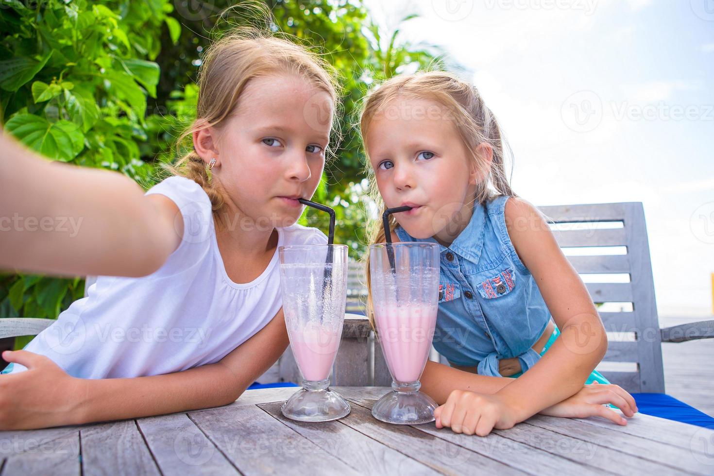 Little girls taking selfie and drinking tasty cocktails at tropical resort photo