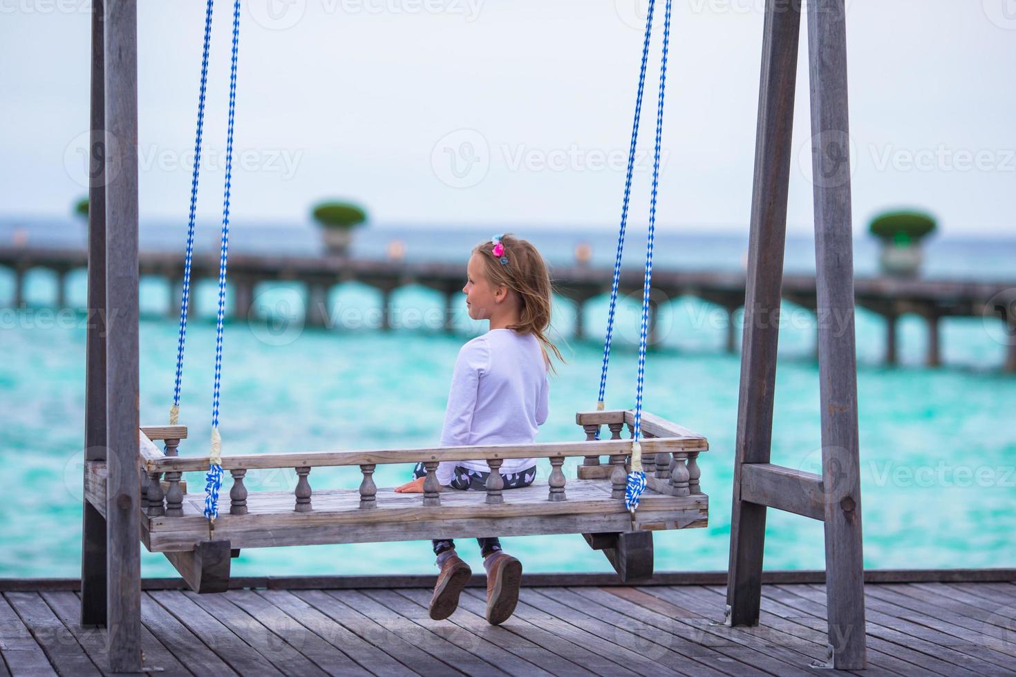 Silhouette of adorable little girl on swing at sunset photo