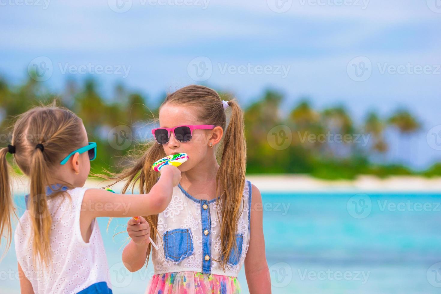 dos niñas comiendo piruletas brillantes en la playa foto