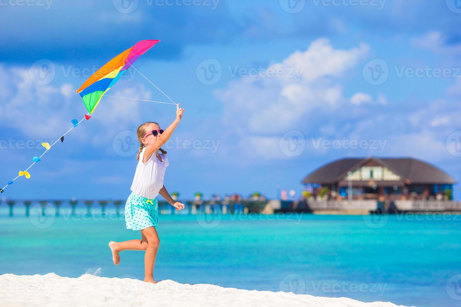 Little happy girl playing with flying kite on tropical beach photo
