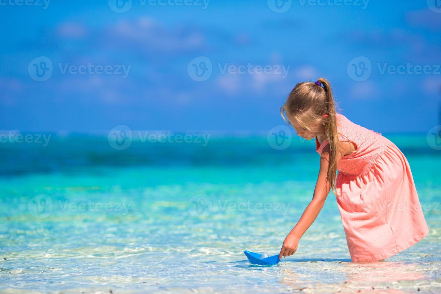 Adorable little girl playing with origami boat in turquoise sea photo