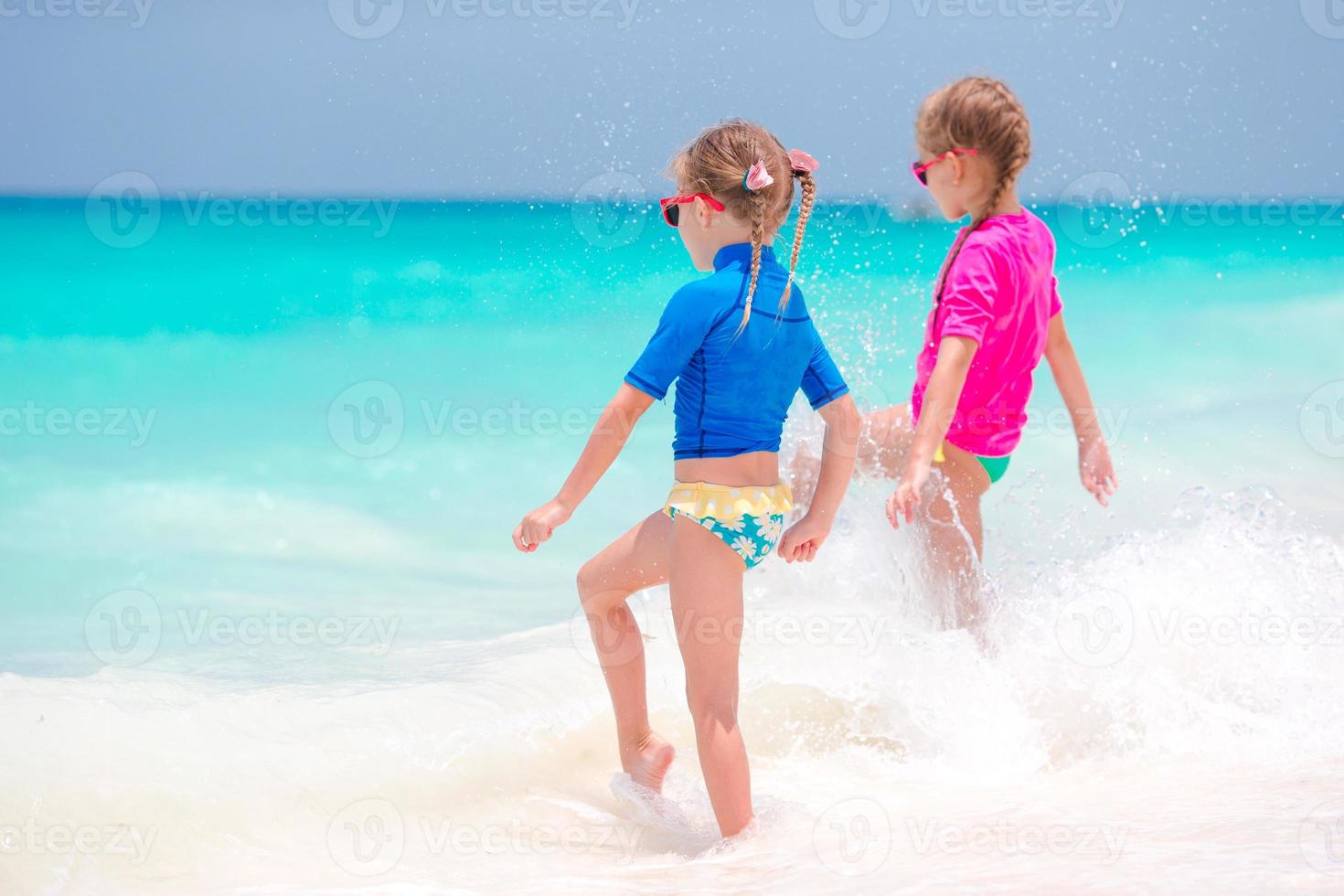 Adorable little girls splashing in tropical shallow water during summer vacation photo