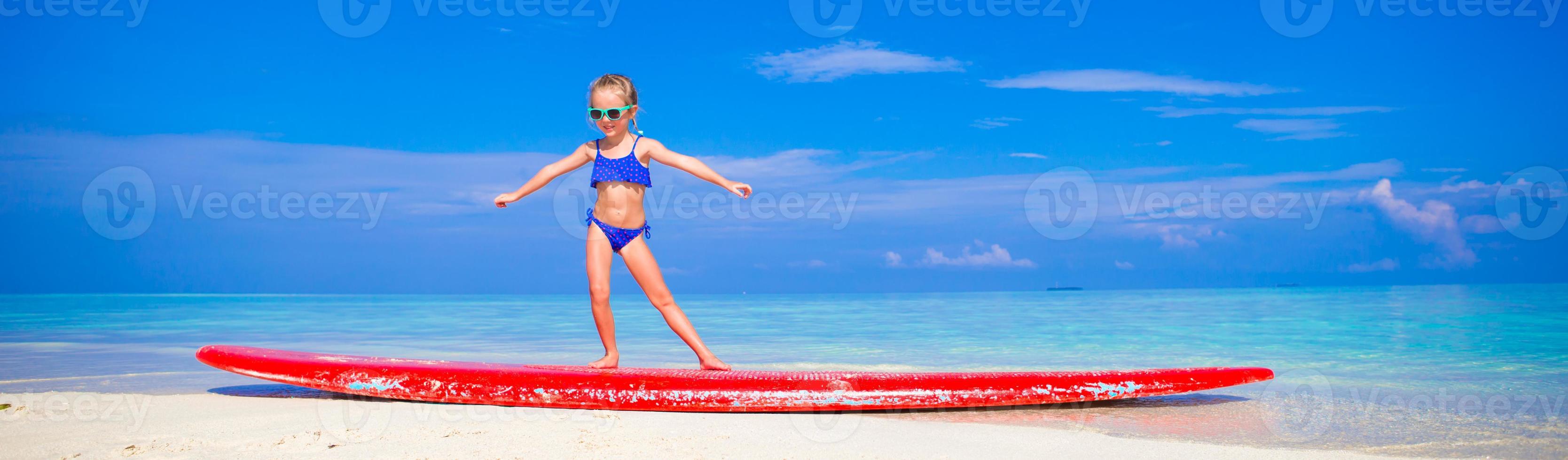 adorable niña practica la posición de surf en la playa foto