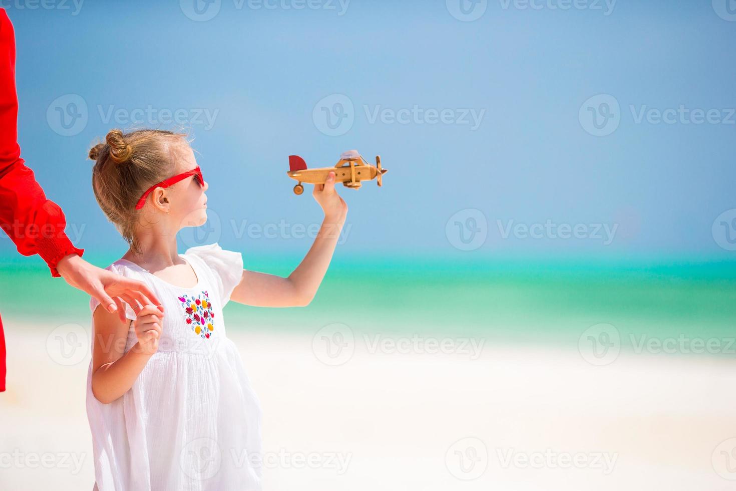 Adorable little girl with toy airplane in hands on white tropical beach photo