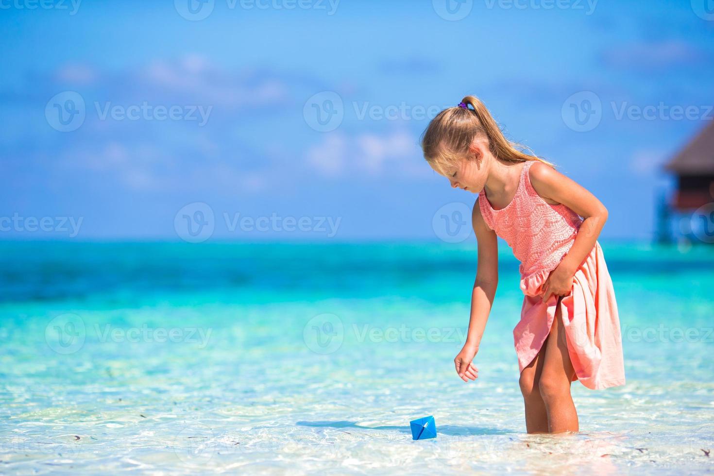 Adorable little girl playing with paper boat in turquoise sea photo