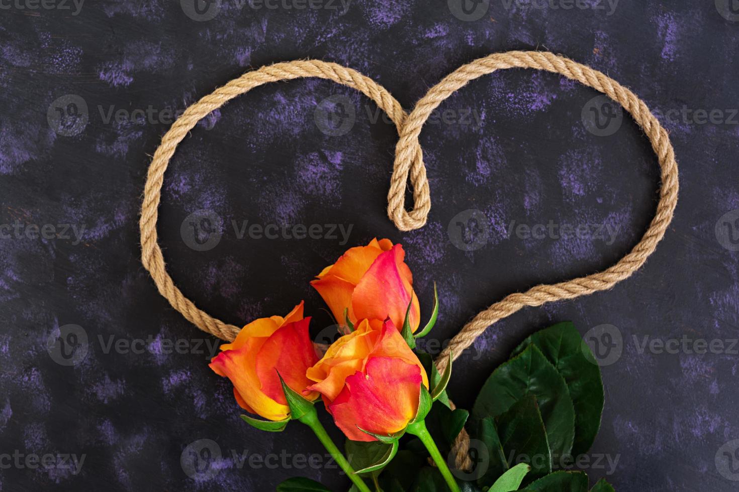 Heart shape made with rope and rose on a dark background. Top view photo