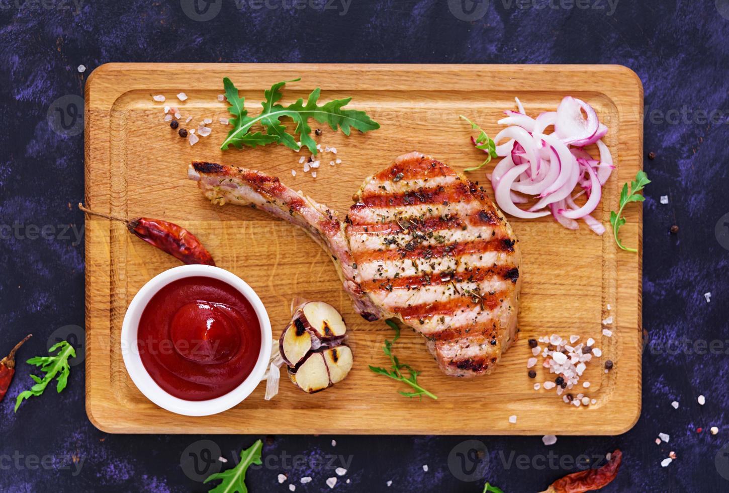 Raw pork steak with herbs on dark background. Raw juicy steak on bone. Top view photo