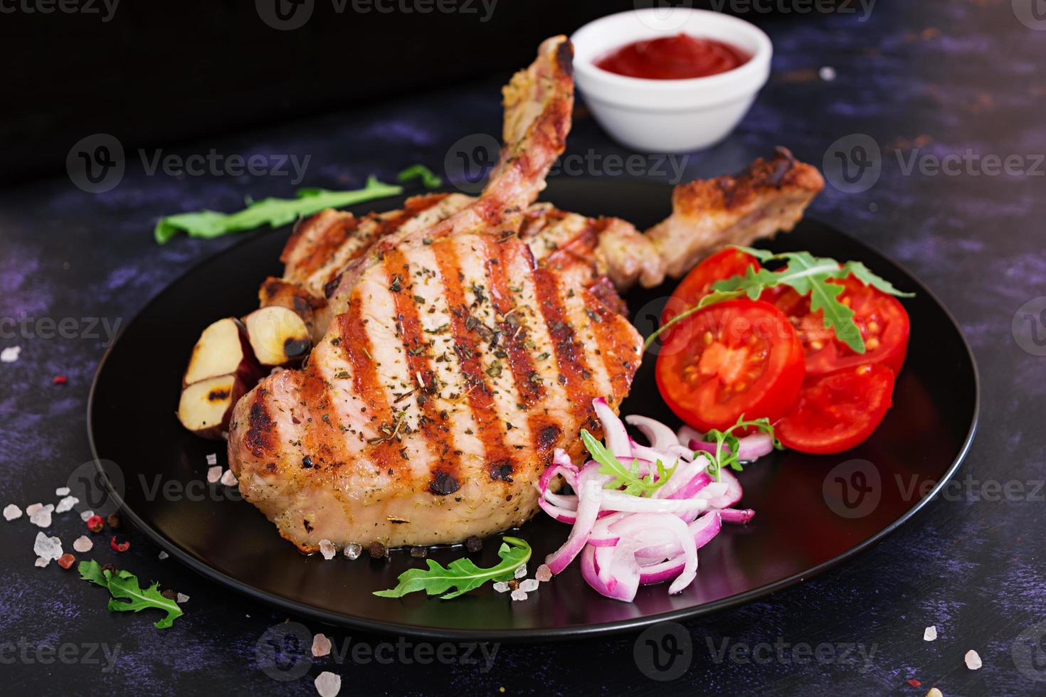 Raw pork steak with herbs on dark background. Raw juicy steak on bone photo