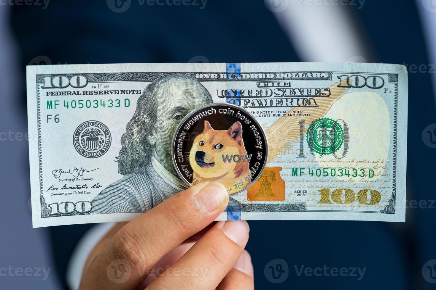 Dogecoin coin DOGE included with Cryptocurrency and stack 100 hundred new US dollar Money American on hand business man wearing a blue suit. Filed and put and give to me. photo