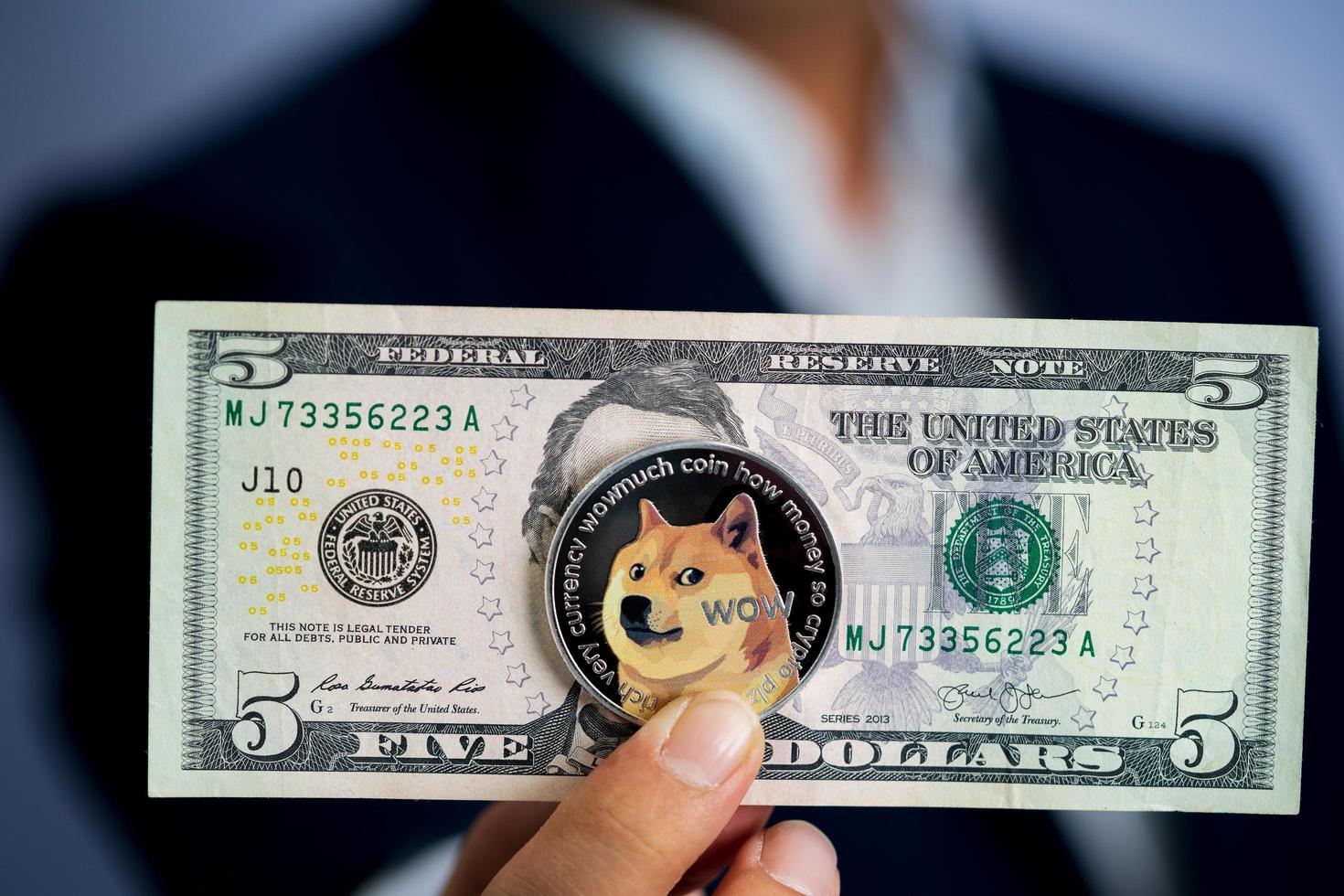 Dogecoin coin DOGE included with Cryptocurrency and stack 5 five US dollar Money American on hand business man wearing a blue suit. Filed and put and give to me. photo