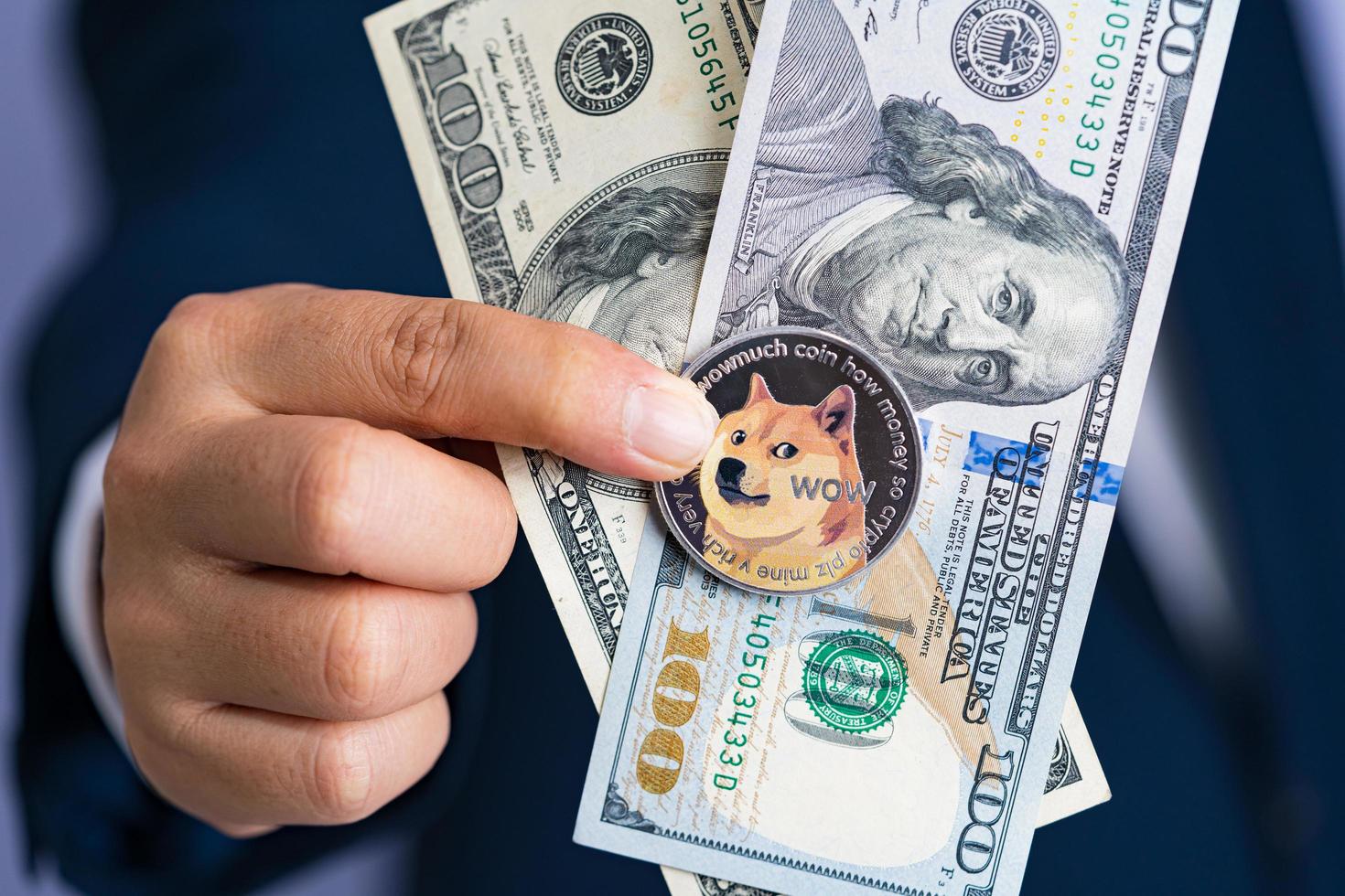 Dogecoin coin DOGE included with Cryptocurrency and stack 100 hundred new US dollar Money American on hand business man wearing a blue suit in the pocket. Filed and put and give to me. photo