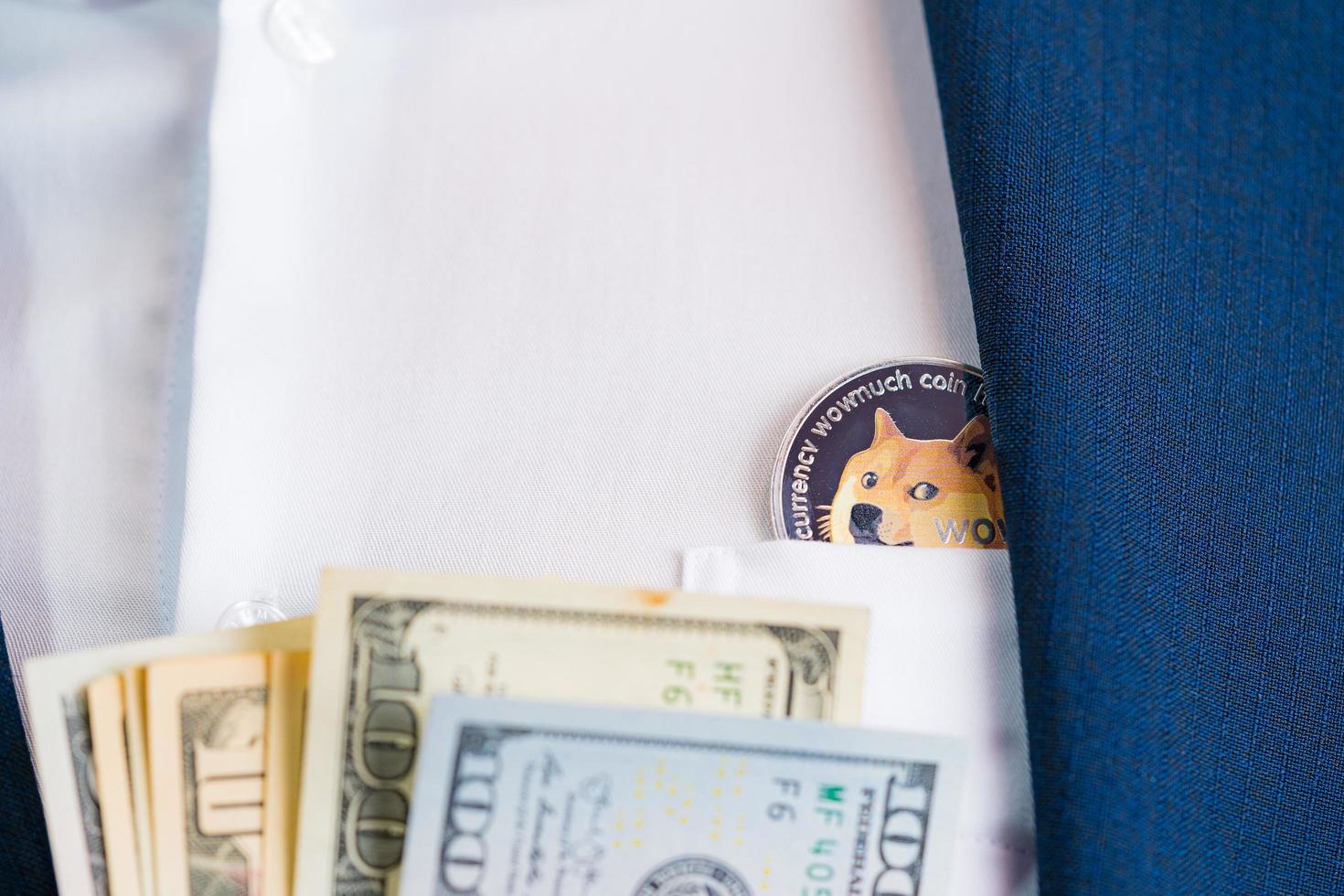 Close up Dogecoin coin DOGE included with Cryptocurrency and stack 100 hundred new US dollar Money American on hand business man wearing a blue suit. Filed and put and give to me. photo