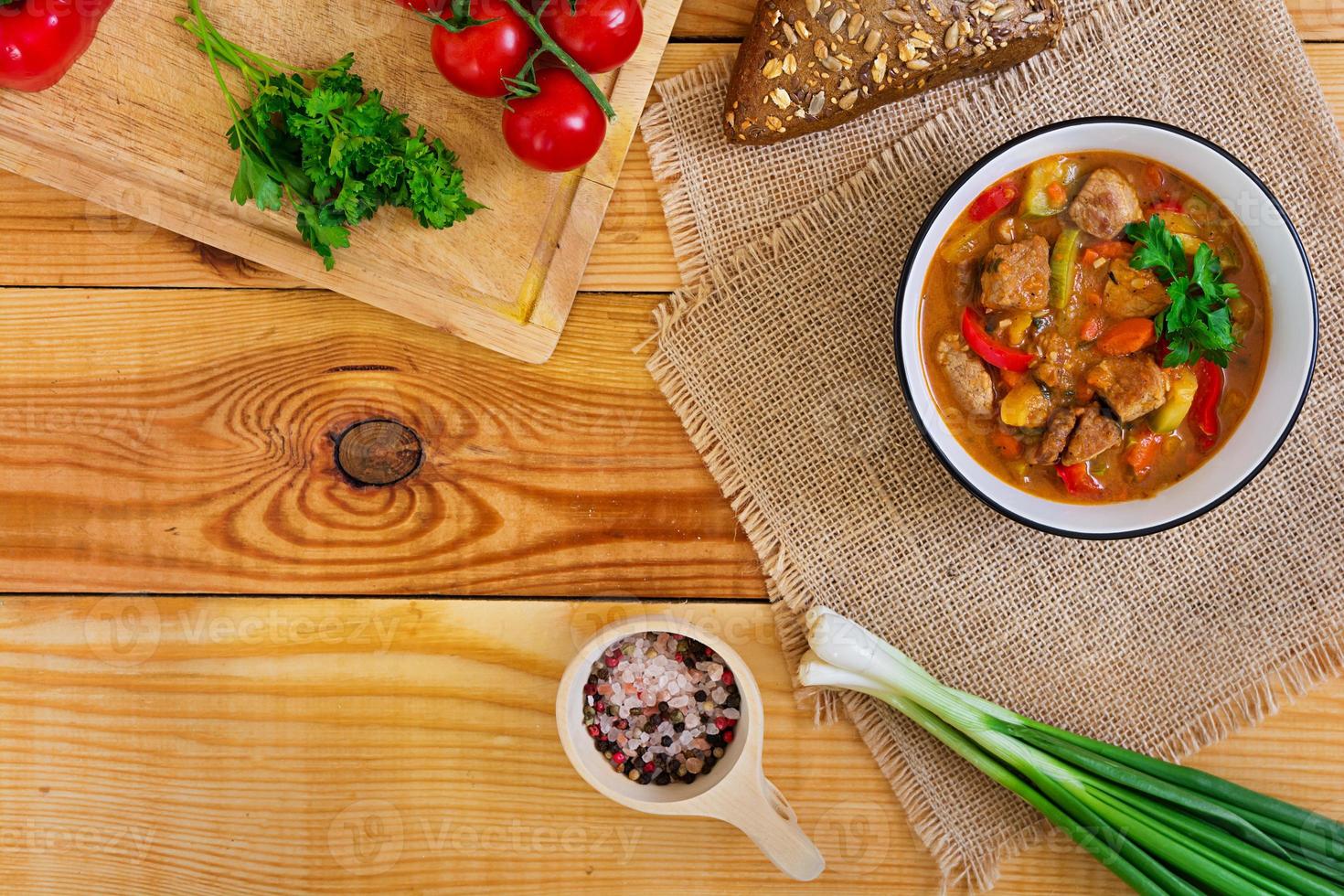 estofado con carne y verduras en salsa de tomate sobre fondo de madera. vista superior foto