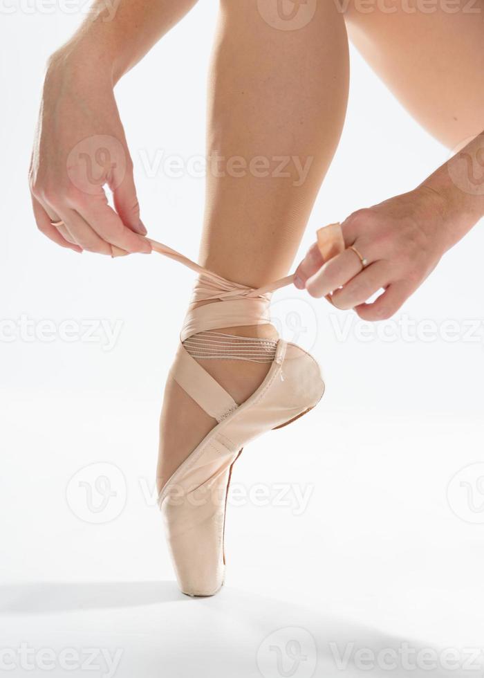 primer plano de hermosas piernas de joven bailarina que se pone zapatos de punta sobre fondo blanco. foto